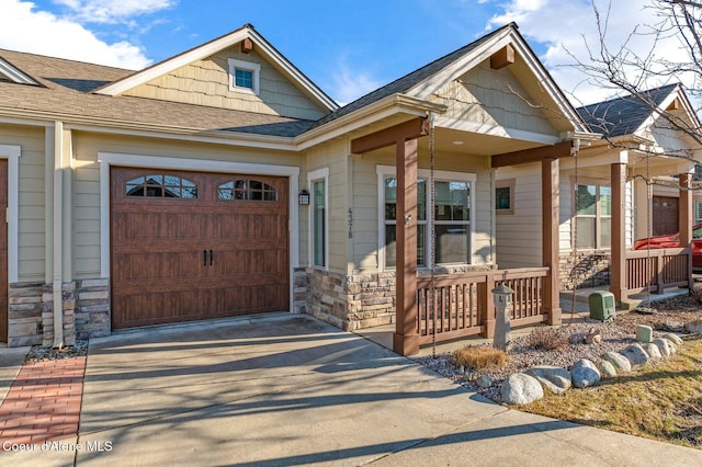 view of front of home with driveway, stone siding, a porch, a shingled roof, and a garage