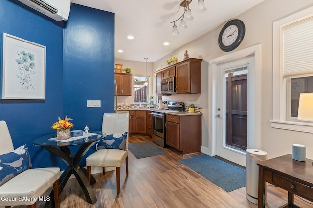 kitchen featuring a wall mounted AC, dark wood finished floors, hanging light fixtures, appliances with stainless steel finishes, and brown cabinets