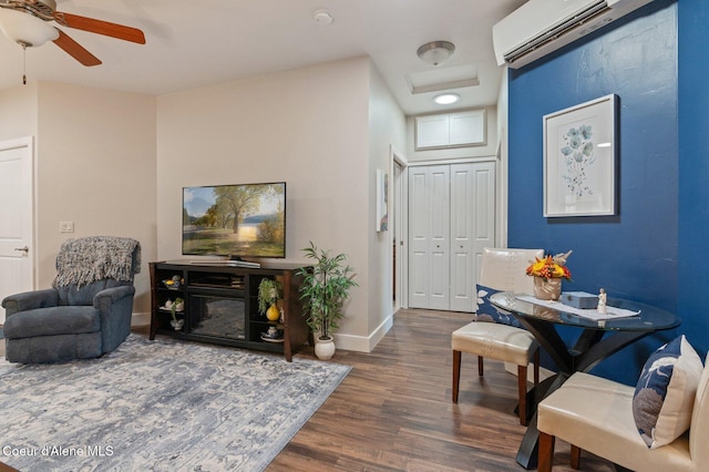 living area with ceiling fan, baseboards, an AC wall unit, and wood finished floors