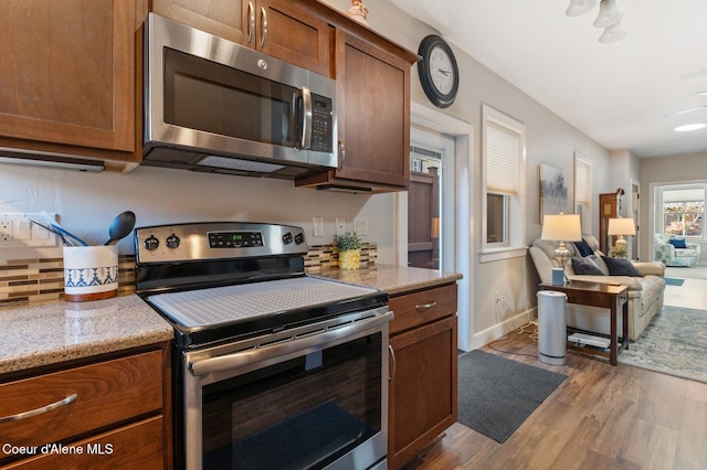 kitchen featuring light stone counters, brown cabinetry, dark wood-style flooring, appliances with stainless steel finishes, and open floor plan