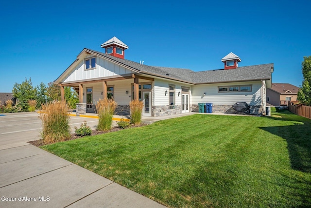 back of house featuring stone siding, a lawn, and board and batten siding