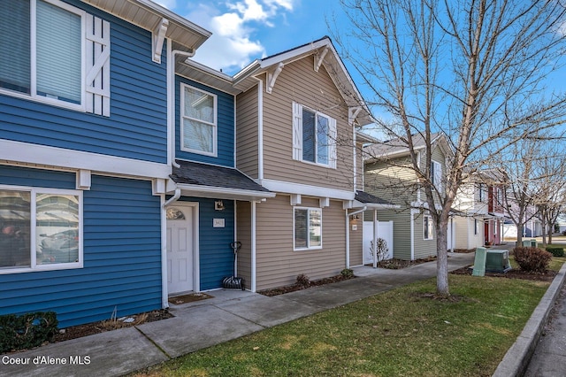 townhome / multi-family property with a residential view, a front lawn, central AC, and roof with shingles