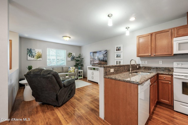 kitchen with open floor plan, a peninsula, wood finished floors, white appliances, and a sink