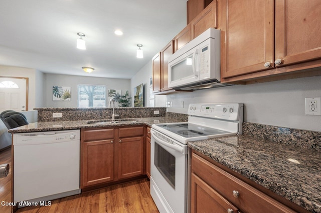 kitchen with light wood finished floors, a peninsula, brown cabinetry, white appliances, and a sink