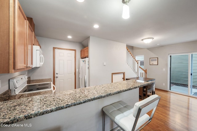 kitchen featuring white appliances, stone counters, light wood finished floors, a breakfast bar, and recessed lighting