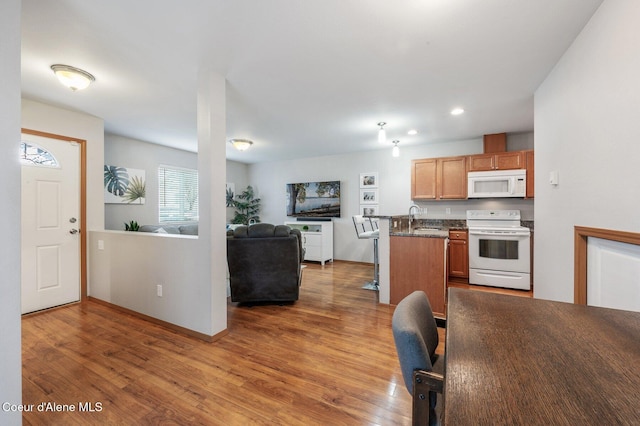 kitchen with a sink, white appliances, wood finished floors, and open floor plan