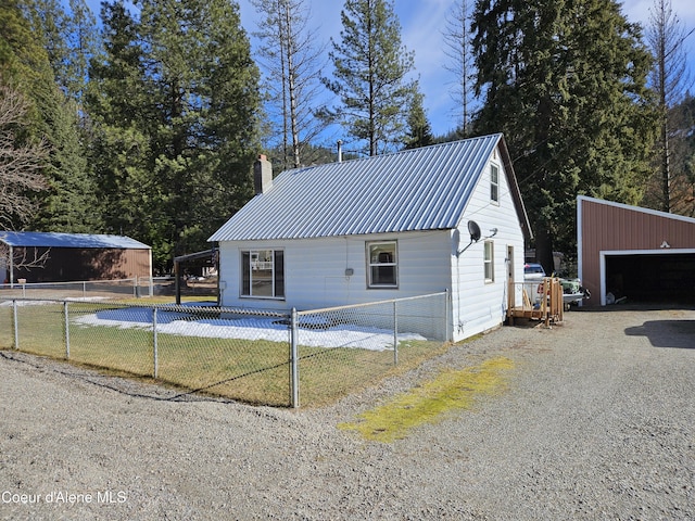 view of side of home with a chimney, metal roof, fence, a garage, and an outdoor structure