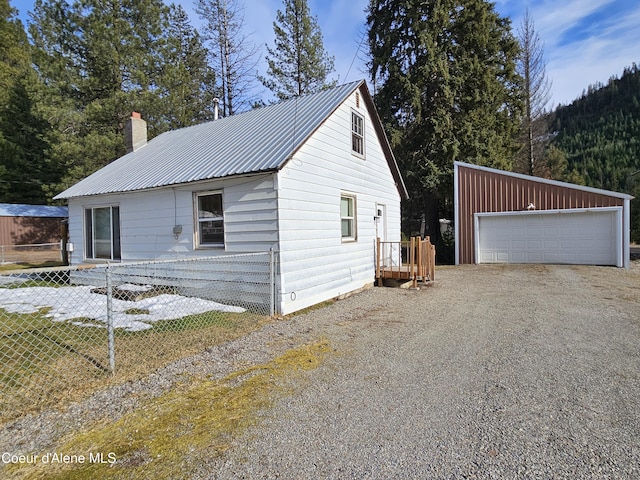 view of home's exterior featuring metal roof, a garage, an outdoor structure, fence, and a chimney