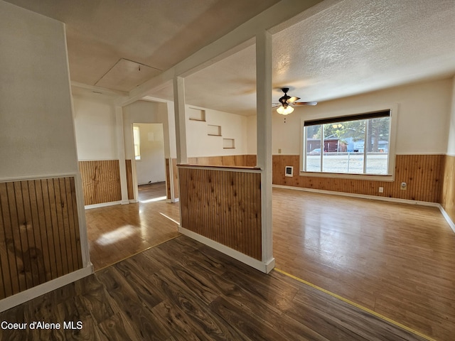 interior space featuring wooden walls, wood finished floors, a textured ceiling, and wainscoting