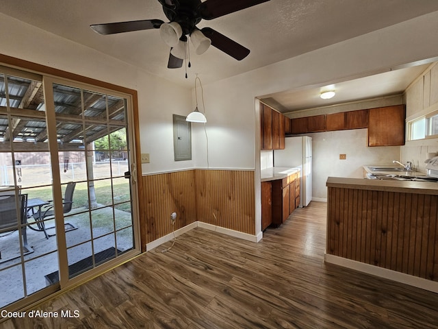 kitchen with dark wood-style flooring, a wainscoted wall, brown cabinetry, freestanding refrigerator, and electric panel