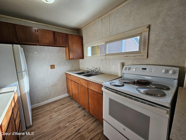 kitchen with white appliances, brown cabinets, wood finished floors, light countertops, and a sink