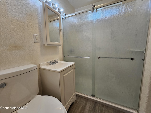 bathroom featuring a textured wall, a shower stall, toilet, and wood finished floors