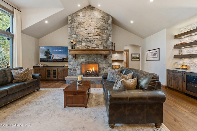 living room with a bar, high vaulted ceiling, wood finished floors, and a stone fireplace