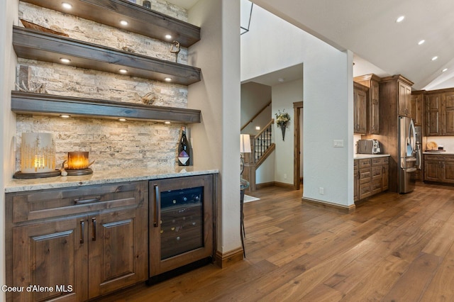 bar with beverage cooler, dark wood-type flooring, vaulted ceiling, stairway, and stainless steel refrigerator