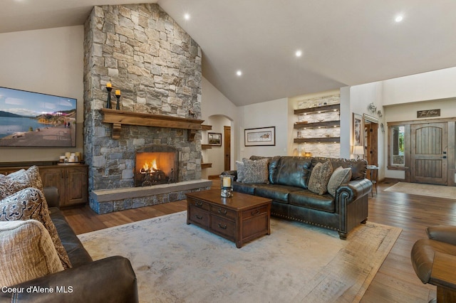 living area featuring high vaulted ceiling, arched walkways, wood finished floors, and a stone fireplace