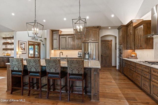 kitchen featuring appliances with stainless steel finishes, decorative backsplash, a large island with sink, and wood finished floors