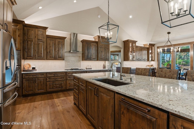 kitchen featuring arched walkways, stainless steel appliances, wall chimney range hood, a chandelier, and a sink