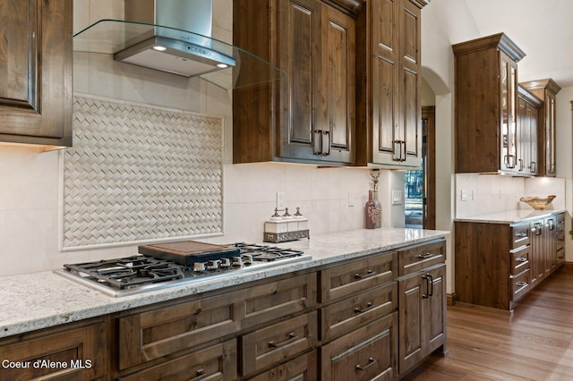 kitchen featuring stainless steel gas cooktop, wall chimney exhaust hood, light stone counters, and dark wood finished floors