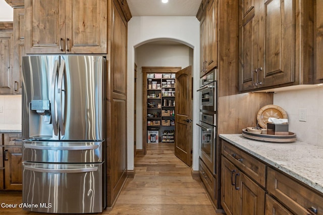 kitchen featuring tasteful backsplash, arched walkways, light wood-style flooring, light stone countertops, and stainless steel refrigerator with ice dispenser