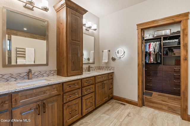 full bath with a sink, backsplash, baseboards, and double vanity