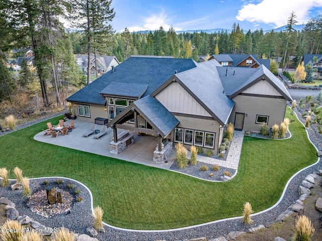 rear view of house featuring a patio, a shingled roof, board and batten siding, and a lawn