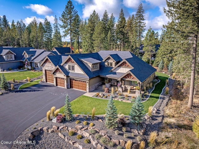 view of front of home featuring a garage, stone siding, aphalt driveway, and a front yard