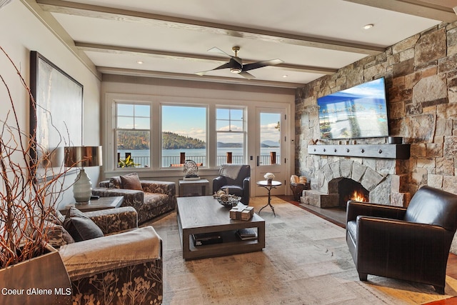 living room featuring beam ceiling, ceiling fan, a stone fireplace, and wood finished floors