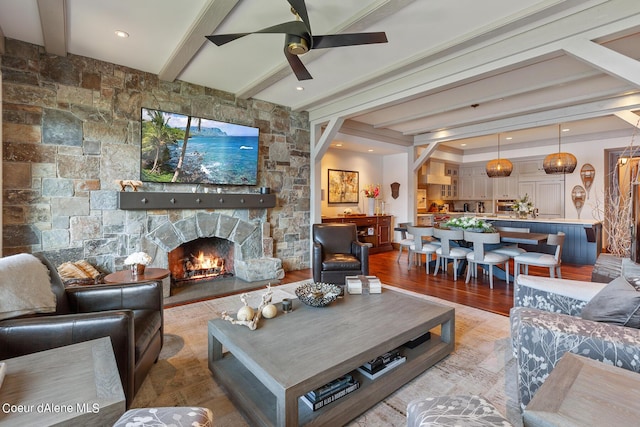 living area with ceiling fan, beamed ceiling, light wood-type flooring, and a fireplace