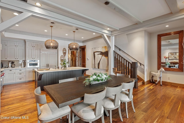 dining space featuring baseboards, stairway, beamed ceiling, and light wood-style floors