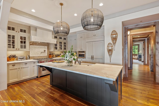 kitchen with premium appliances, a center island with sink, decorative backsplash, dark wood-type flooring, and extractor fan