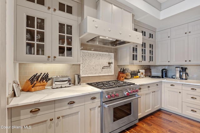 kitchen featuring light stone countertops, backsplash, wood finished floors, luxury stove, and under cabinet range hood