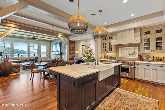 kitchen with open floor plan, wall chimney exhaust hood, luxury range, and a sink