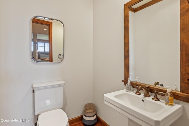 half bath with baseboards, a sink, and toilet