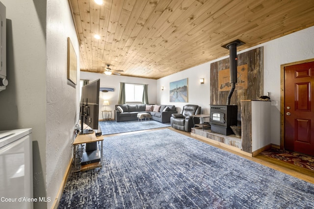 living room featuring a ceiling fan, wood finished floors, wooden ceiling, a wood stove, and a textured wall