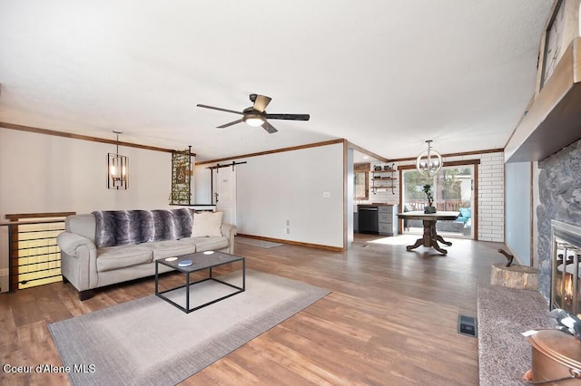 living room featuring a glass covered fireplace, a barn door, wood finished floors, and ornamental molding