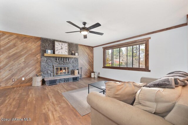 living room with a stone fireplace, wooden walls, wood finished floors, and ceiling fan