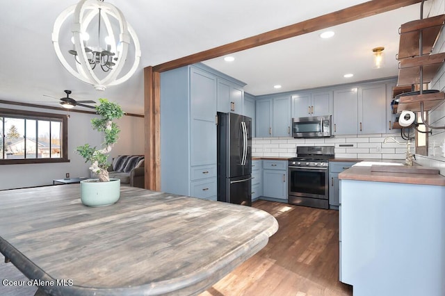 kitchen with blue cabinetry, dark wood-style flooring, a sink, decorative backsplash, and appliances with stainless steel finishes