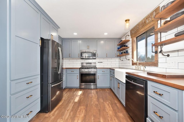 kitchen featuring open shelves, a sink, tasteful backsplash, wood finished floors, and appliances with stainless steel finishes