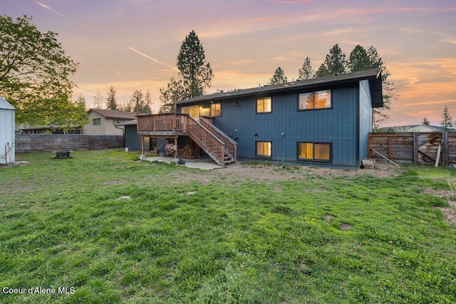 back of house at dusk with stairway, a lawn, a fenced backyard, and a deck