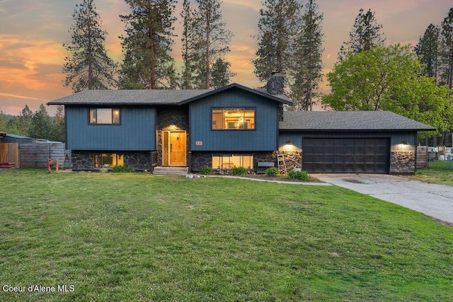 raised ranch with stone siding, a lawn, and an attached garage