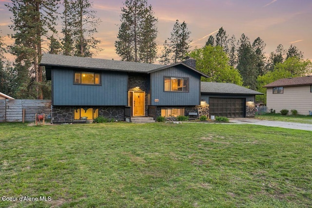 split foyer home featuring a front yard, fence, driveway, a garage, and stone siding