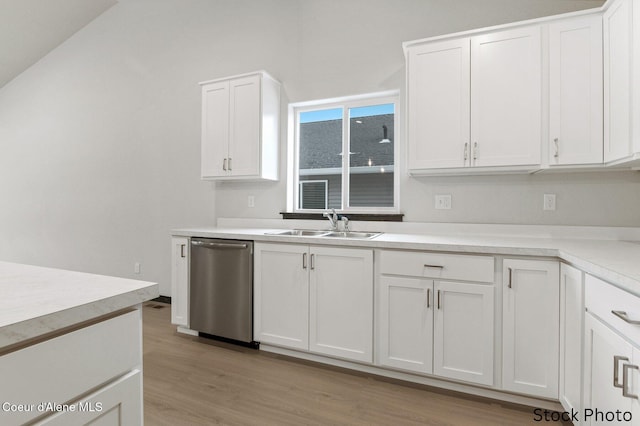 kitchen with light countertops, light wood-style flooring, stainless steel dishwasher, white cabinets, and a sink