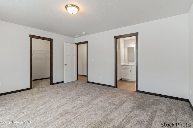 unfurnished bedroom with baseboards, a spacious closet, a textured ceiling, carpet floors, and a closet