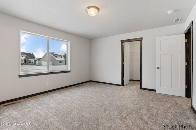 unfurnished bedroom with a textured ceiling, carpet flooring, and visible vents