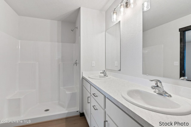 full bath featuring double vanity, a sink, a textured ceiling, and walk in shower