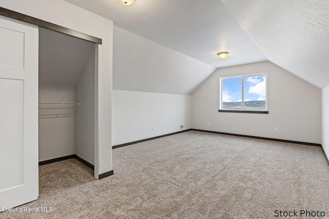 additional living space with a textured ceiling, vaulted ceiling, carpet, and baseboards