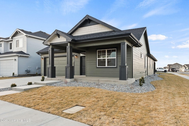 view of front of home featuring roof with shingles, covered porch, a front yard, a garage, and driveway