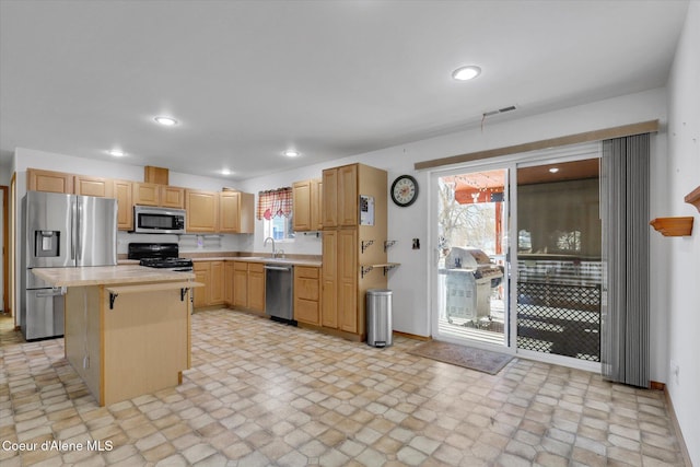 kitchen with a kitchen island, appliances with stainless steel finishes, light countertops, and a sink