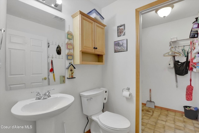 bathroom featuring baseboards, visible vents, toilet, tile patterned floors, and a sink