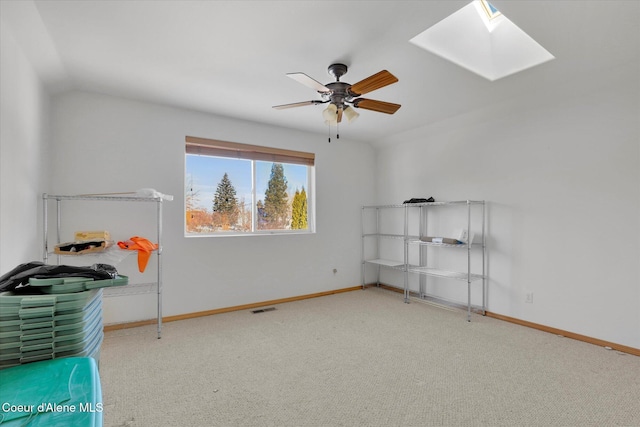 interior space featuring a skylight, baseboards, visible vents, ceiling fan, and carpet flooring